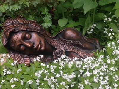 Sculpture d’argile femme coucher dans un fond vert fleurie